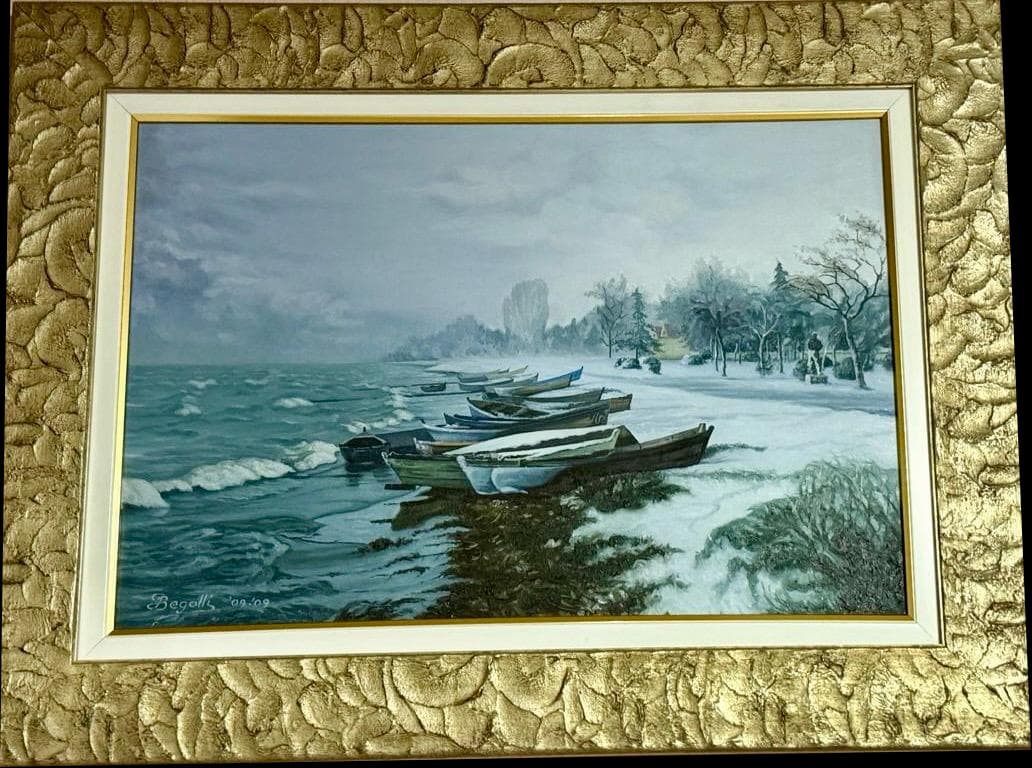Small wooden boats beside a snowy shoreline beneath a grey sky, in an ornate gold frame
