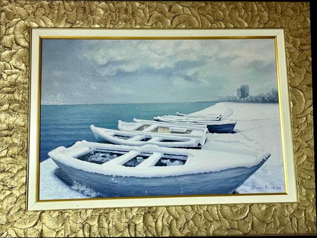 A row of small boats filled with snow beside quiet blue water, in a textured gold frame